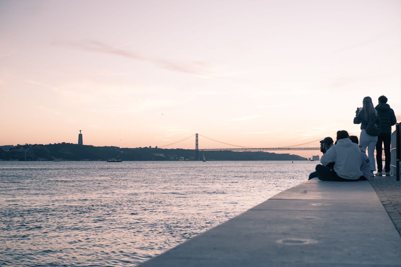 Personnes assises au bord du Tage à Lisbonne au coucher du soleil